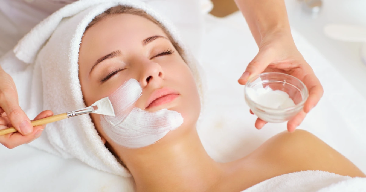 Woman receiving professional facials treatment in Bend, OR, with a skincare specialist applying a cream mask using a brush.
